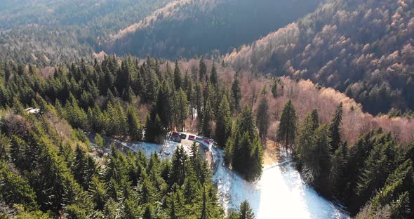 Aerial, tilt down, drone shot, of a car on a winding, hillside road, in Romanian forest, on a mounta