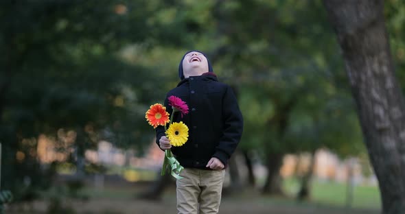 Little Boy is Standing and Waiting in a Park with Flowers
