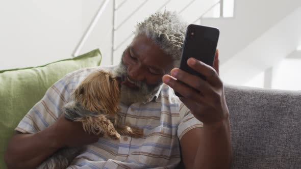 Senior man holding his dog having a video chat on smartphone at home