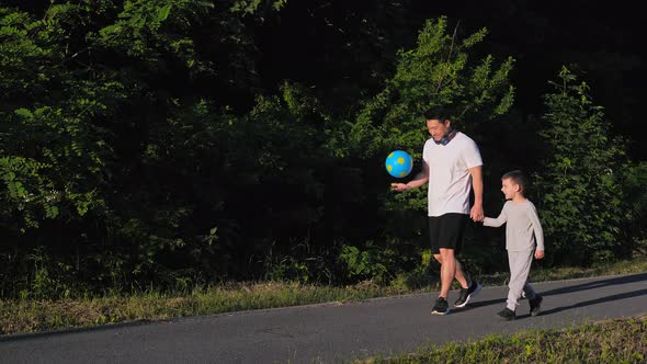 Asian Man with Ball Holding Baby's Hand Going to Workout at Sunset