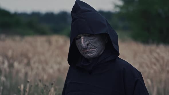 Close-up scary face of ghost. Nightmare in black costume with hood looking at camera