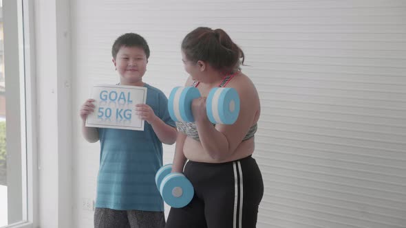 Asian family with mother in sportswear lifting dumbbell and son cheer with goal for diet.