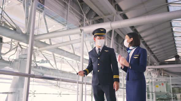 Airliner pilot and air hostess wear protective face mask walking in airport terminal to the airplane