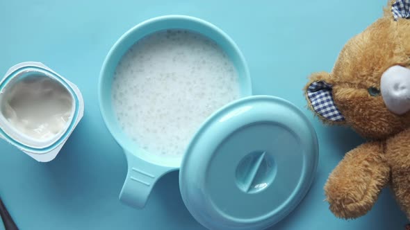 Baby Food in a Bowl and Yogurt in a Container on Blue Background