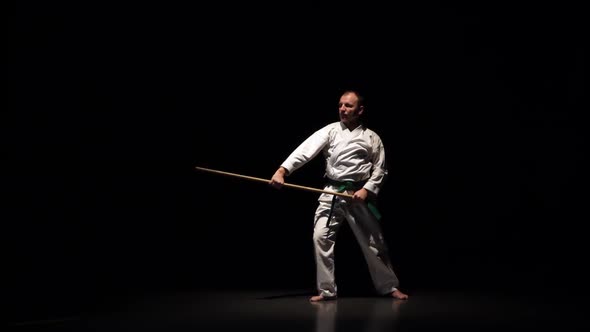 Kendo Fighter on White Kimono Practicing Martial Art with the Bamboo Bokken on Black Background