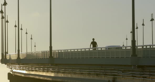 Silhouette of Person Riding Electric Scooter on Bridge on Golden Hour Sunlight