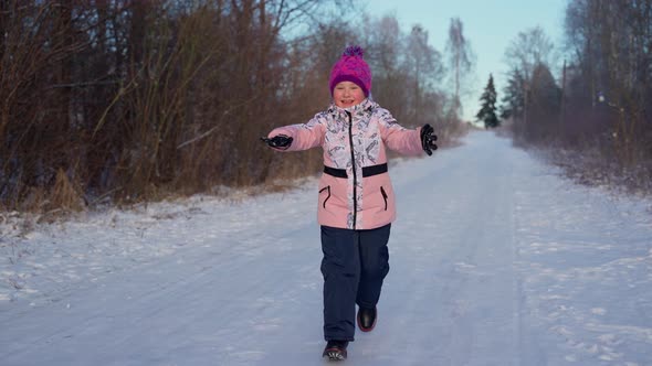 Happy child running looking at camera at winter woods outdoors. Cute female girl with open hands