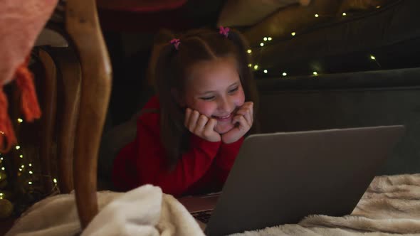 Caucasian girl smiling while using laptop under blanket fort during christmas at home