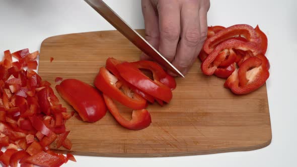 Male Cook Chopping Red Bell Pepper with Knife into Small Slices on Wooden Kitchen Cutting Board