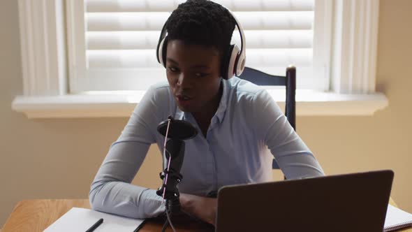 African american woman wearing headphones talking in microphone while looking at laptop