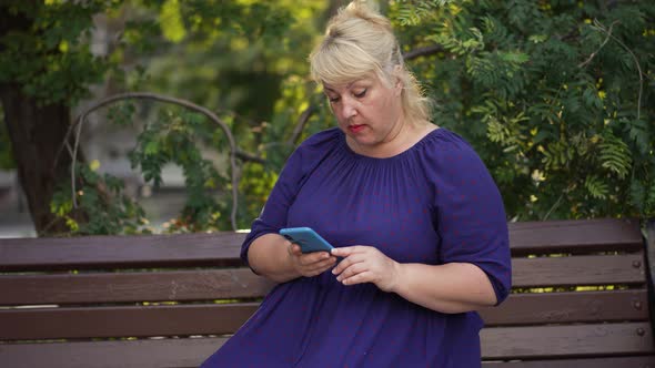 Fat Woman Uses Smartphone Sitting on a Bench