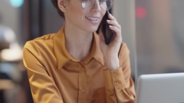 Caucasian Female Freelancer with Laptop Chatting on Mobile Phone in Cafe