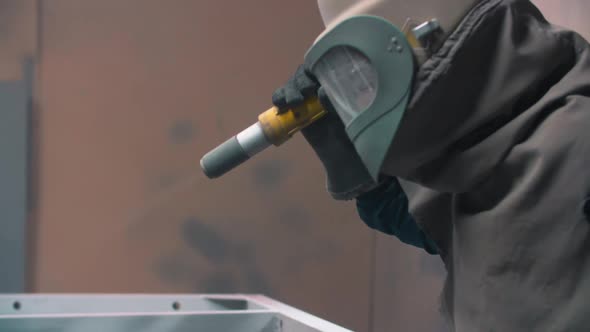 worker wearing mask using sand blast on metal surface in workshop