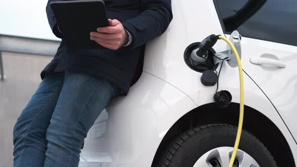 Man Using a Tablet and Waiting for Charging of Electric Car