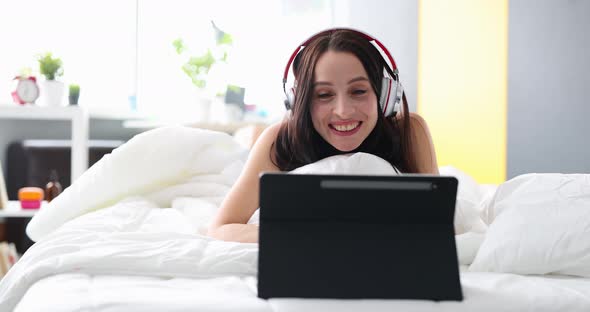 Joyful Woman in Headphones Communicates By Video Call While Lying in Bed