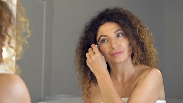 Wellgroomed Mature Woman Combing Her Eyebrows with Brow Brush in Front of the Mirror