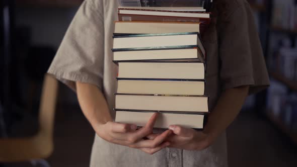 Unrecognizable Student Walks with Plenty of Books in the Library Preparing for Exams