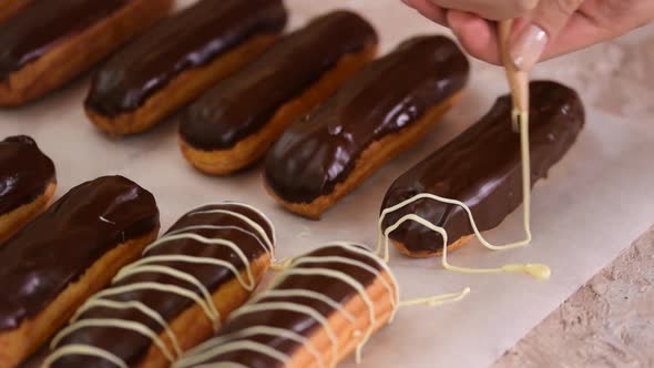 Pastry chef pours white chocolate on French eclairs.