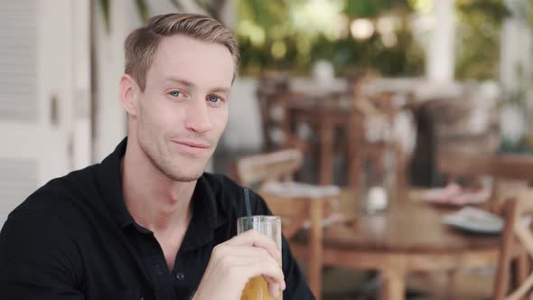 Portrait of Blond Man Drinking Fresh Juice in Cafe, Looks at Camera, Smiles