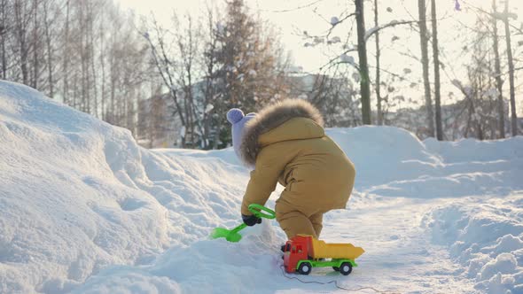 A kid of 15-23 months digs snow with a toy shovel.