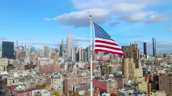 Slow Motion Aerial orbiting around USA flag waiving with blue sky and Manhattan in the background.