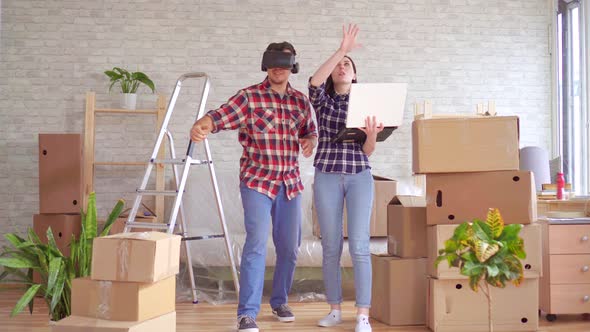 Young Woman with a Laptop Shows a Man in VR Glasses the Project of a New Apartment