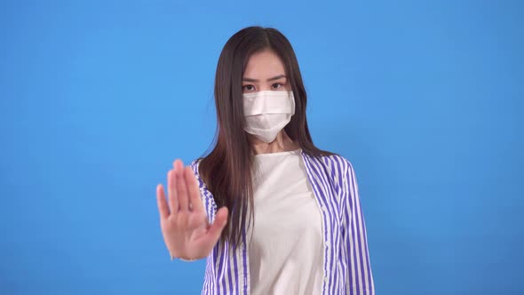 Young Asian Woman with a Protective Medical Mask on Her Face Shows a Stop Gesture While Standing on