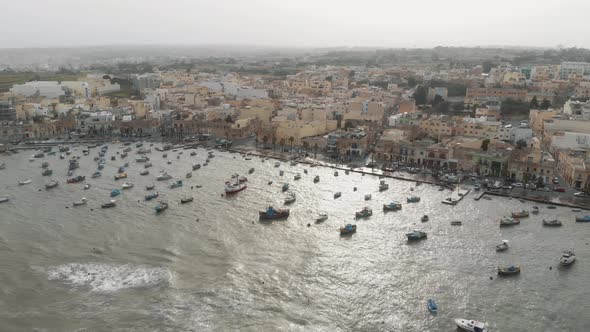 Aerial Wide Pan Right Shot Of Marsaxlokk Port With Village Background In Malta