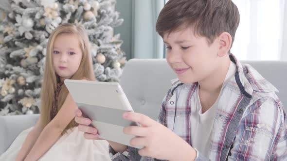 Side View of Happy Caucasian Boy Sitting with Tablet and Smiling, Pretty Girl Looking at Him at the