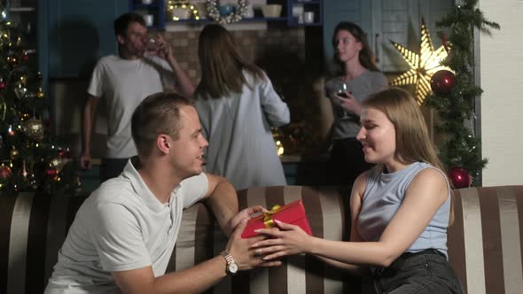 Man and woman sit in decorated room and give each other gifts for Christmas