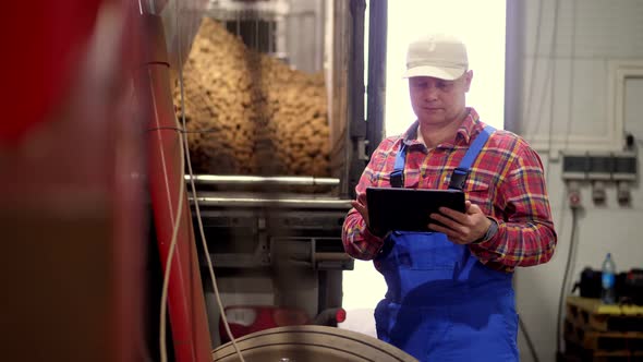 Farmer with Tablet in Potato Storage Warehouse. Background of Loading Potatoes Into Truck, Using