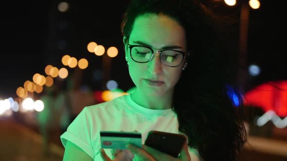 Pretty Woman Stands on the Street in a White T-shirt and Glasses, Makes Online Payments By Credit