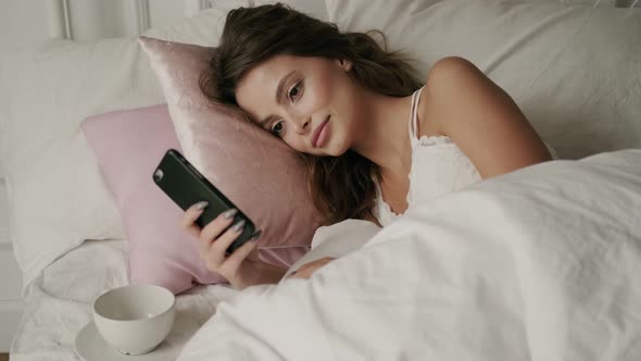 Close Up of Sexy Young Woman in Pajamas Resting with Mobile Phone in Home Bedroom, Pin-up Girl