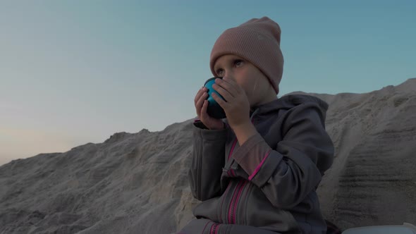 Little girl sitting on a sandy beach and sipping tea