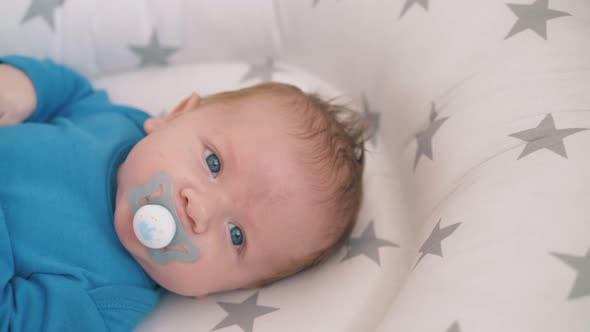 Cute Kid with Blue Eyes Sucks Pacifier in Cocoon at Home