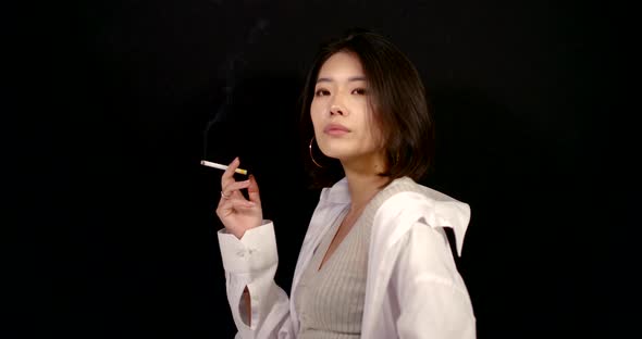 Portrait in Profile of a Young Asian Woman in a White Shirt and with Large Ring Earrings on a Black