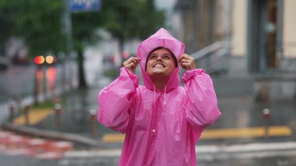 Young Smiling Woman with a Pink Raincoat While Enjoying a Walk Through the City on a Rainy Day