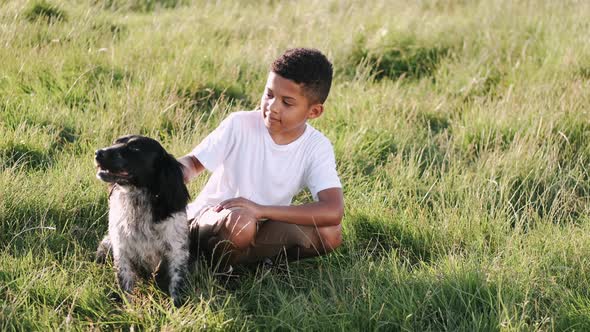 African Boy with Dog Sitting in the Grass on Sunset