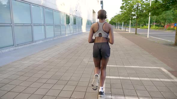 Slow motion shot of young woman with headphones jogging in city