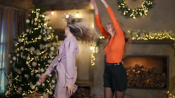 Two Blondes in Festive Clothes are Laughing and Jumping Merrily Against the Background of a Room