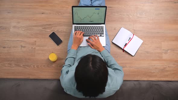 Overhead View of Multiracial Freelancer Sitting at the Floor and Typing on the Laptop