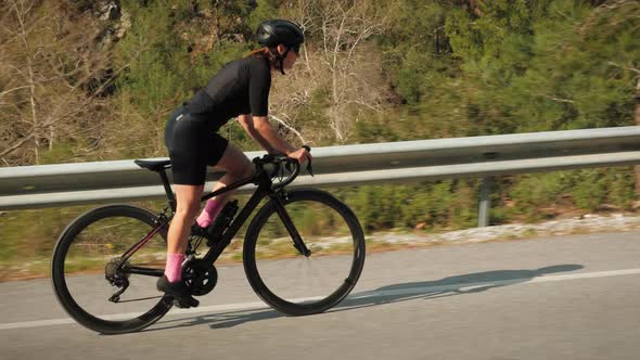 Fit sportive woman climbing up on road bicycle through mountain hill.