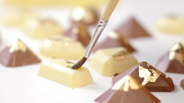 Close-up Decorating White and Milk Chocolate Candies with Gold Foil Using Brush