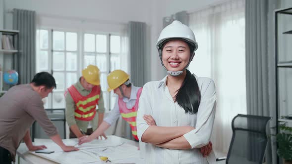 Woman Engineer With Helmet Crossing Arms And Smiling To Camera While His Colleagues Working