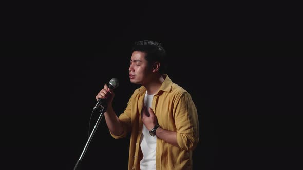 Side View Of Asian Man Singer Singing Into Microphone On Black Background