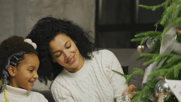 Portrait of Happy African American Mom and Little Daughter Decorate Christmas Tree with Festive Toys