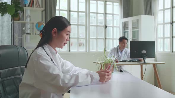 Asian Woman Doctor Having Video Conference On Tablet Computer In Workplace With Patient