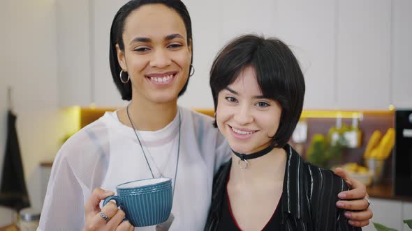 Closeup of Happy Lesbian Couple is Drinking Coffee in the Kitchen Embracing