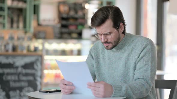 Young Man Reacting to Loss While Reading Papers