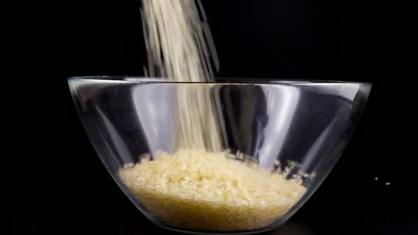 Rice is poured into a glass bowl on a black background